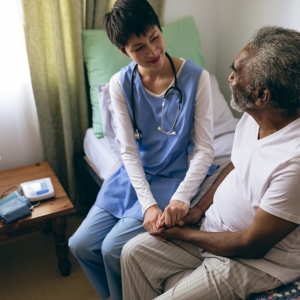 High angle view of Asian female doctor and senior male patient interacting with each other at retirement home. They are holding hands.