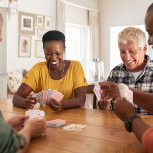 Retired multiethnic people playing cards together at home. Happy senior friends with african couple playing cards. Cheerful active seniors playing game at lunch table.